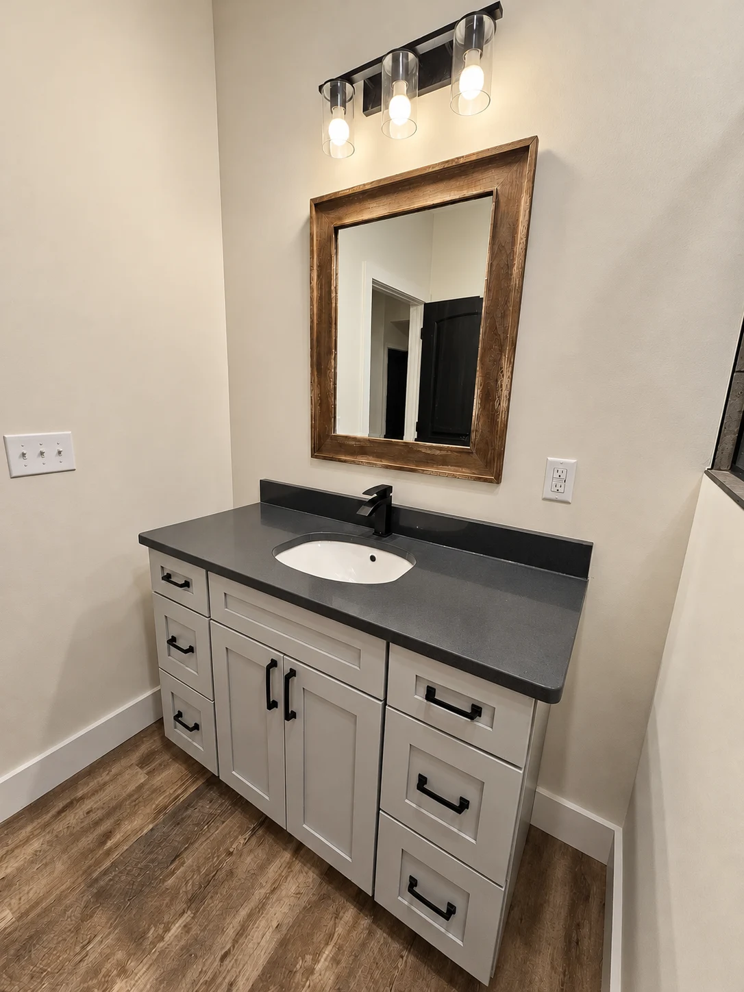 Gray shaker vanity with dark counter and wood-framed mirror